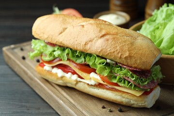 Delicious baguette sandwich with salami and cheese on grey wooden table, closeup