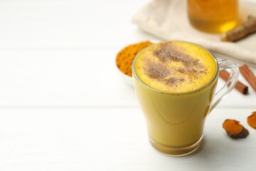 Tasty turmeric latte in cup and ingredients on white wooden table, closeup. Space for text