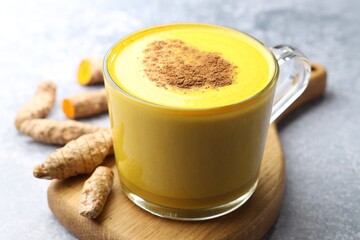 Tasty turmeric latte in cup and roots on grey table, closeup