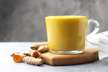 Tasty turmeric latte in cup and roots on grey table, closeup