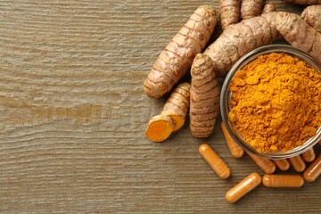 Turmeric capsules, powder and roots on wooden table, flat lay. Space for text