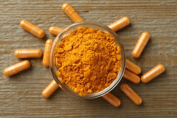 Turmeric capsules and powder on wooden table, flat lay