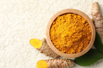 Turmeric powder in bowl, roots and leaves on light textured table, flat lay. Space for text