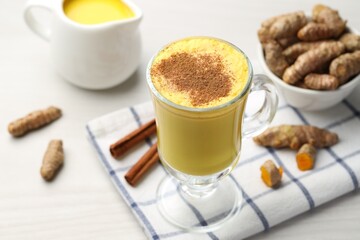 Delicious turmeric latte and rhizomes on white wooden table, closeup