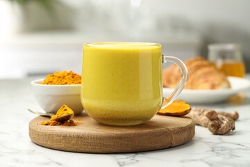 Delicious turmeric latte, powder and rhizomes on white marble table, closeup