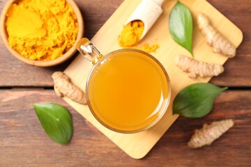 Aromatic turmeric tea in glass mug, roots, powder and green leaves on wooden table, flat lay