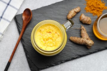 Delicious turmeric latte with honey, powder and rhizomes on grey table, flat lay
