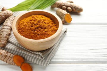 Aromatic turmeric powder, fresh roots and leaves on white wooden table, closeup. Space for text
