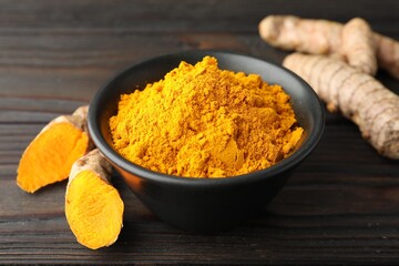 Aromatic turmeric powder in bowl and fresh roots on wooden table, closeup