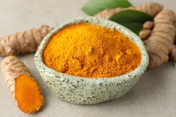 Aromatic turmeric powder in bowl, fresh roots and leaves on light grey table, closeup