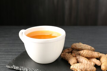 Aromatic turmeric tea and rhizomes on black table, closeup