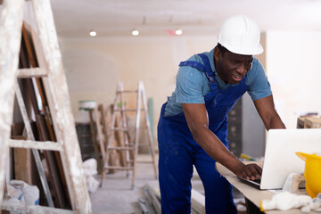 Focused african american engineer working on an construction site indoors checks a home renovation plan on a laptop