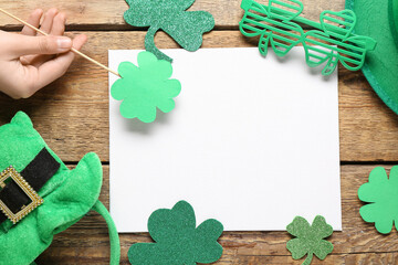 Female hand with blank card, leprechaun hat and paper clovers on wooden background. St. Patrick's...