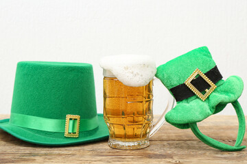 Mug of beer with leprechaun hats on wooden table against white background. St. Patrick's Day...