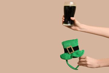 Hands with beer and party decor in shape of leprechaun's hat on beige background. St. Patrick's Day...