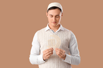 Young Muslim man with decorative crescent on beige background. Ramadan celebration