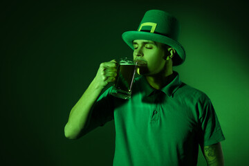 Young man drinking beer on dark green background. St. Patrick's Day