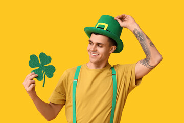 Happy young man in leprechaun's hat and with clover on yellow background. St. Patrick's Day