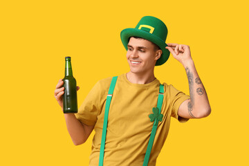 Happy young man in leprechaun's hat and with bottle of beer on yellow background. St. Patrick's Day