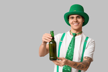 Happy tattooed young man in leprechaun's hat and with bottle of beer on light background. St....