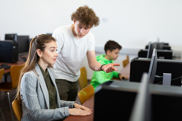Young boy asking teacher about computer problem during computer science lesson.