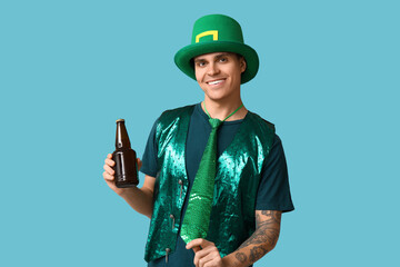 Happy young tattooed man in green clothes and with bottle of beer on blue background. St. Patrick's...
