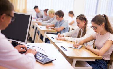 Smart teenagers studying in classroom, listening to lecturer and writing in notebooks