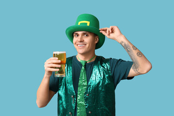 Happy young tattooed man in green clothes and with glass of beer on blue background. St. Patrick's...