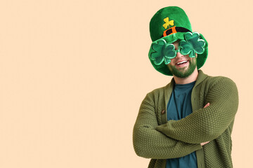 Young man in leprechaun hat and decorative glasses in shape of clover with green beard on beige...