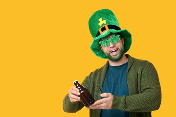 Young man in leprechaun hat and decorative glasses in shape of clover with green beard holding...