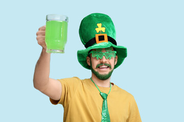 Young man in leprechaun hat and decorative glasses in shape of clover with green beard holding...