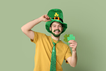 Happy young man in leprechaun hat with green beard holding clover on green background. St....
