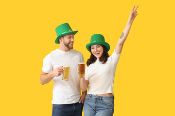 Happy young couple in leprechaun hats with glasses of beer on yellow background. St. Patrick's Day celebration