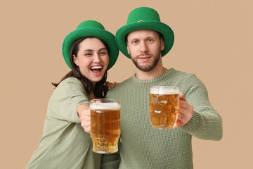 Beautiful young couple in leprechaun hats with glasses of beer on brown background. St. Patrick's...