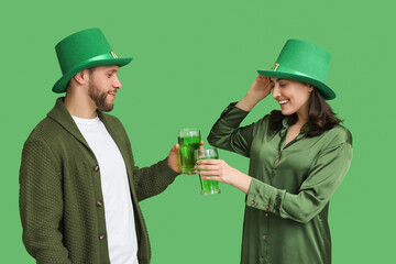 Beautiful young couple in leprechaun hats with glasses of beer on green background. St. Patrick's Day celebration