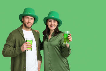 Happy young couple in leprechaun hats with glasses of beer on green background. St. Patrick's Day...