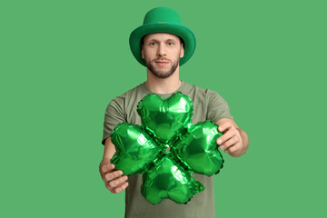 Young man in leprechaun hat with air balloon in shape of clover on green background. St. Patrick's...
