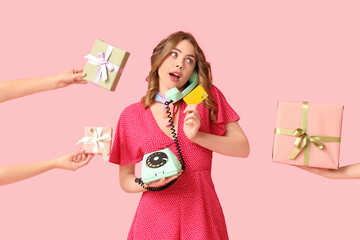 Young woman talking by retro telephone with credit card and hands holding gift boxes on pink background. International Women's Day