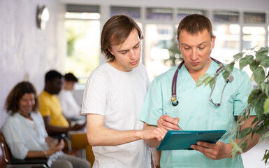 Obraz premium Doctor consults a man undergoing medical examination at the clinic, showing him the test results on paper