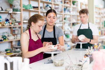 Woman master potter teaches teen girl how to draw and glaze pottery