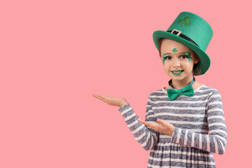Funny girl with face painting and leprechaun's hat showing something on pink background. St....
