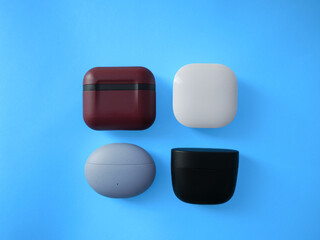 A minimalist flat lay featuring four wireless earbud cases arranged in a neat grid on a vibrant blue background. The cases come in four distinct colors, each showcasing a unique texture and finish.