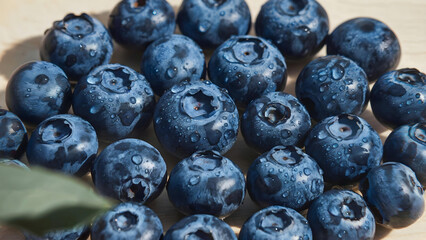 Fresh blueberries with drops of water spread on a light-colored wooden surface create a juicy and appetizing appearance, emphasizing the naturalness and benefits of this superfood