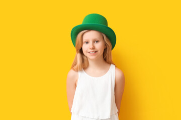 Cute little girl in leprechaun hat on yellow background. St. Patrick's Day celebration