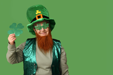 Senior woman in leprechaun hat and decorative glasses with red beard holding clover on green...