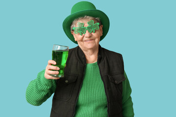 Senior woman in leprechaun hat and decorative glasses with glass of beer on blue background. St....