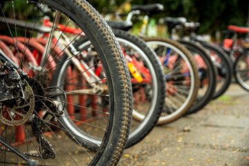 Close-up of a mountain bike with the rim covered in mud, highlighting the details of the spokes and disc brake. In the background several bicycles lined up in a parking lot.  