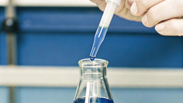 A closeup shot of a scientists hands carefully pipetting a bright blue dye into a flask showcasing the precise technique required in cell culture techniques.