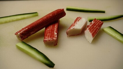 Crab sticks layout. Sliced cucumber pieces. White cutting board. Sushi ingredient concept.


