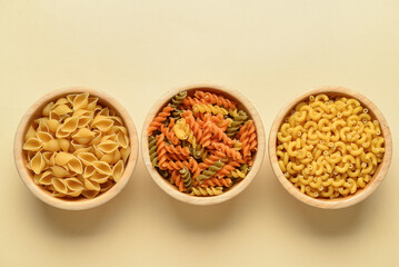 Bowls with different tasty uncooked pasta on beige background